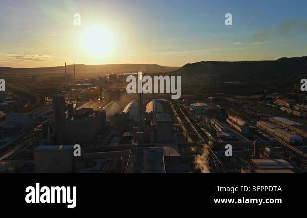 Large Area Sunset casts light over a large industrial area with factories, smoke ...