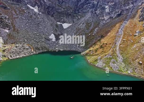 Large Area A small boat moves slowly on a green lake located in a mountainous area ...