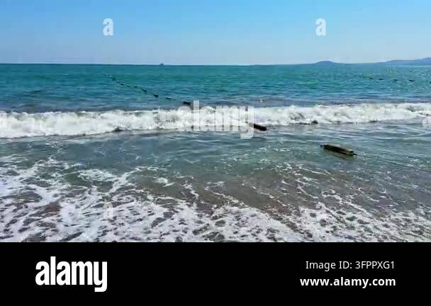 Waves are hitting the sand along the beach. The water is blue and calm ...
