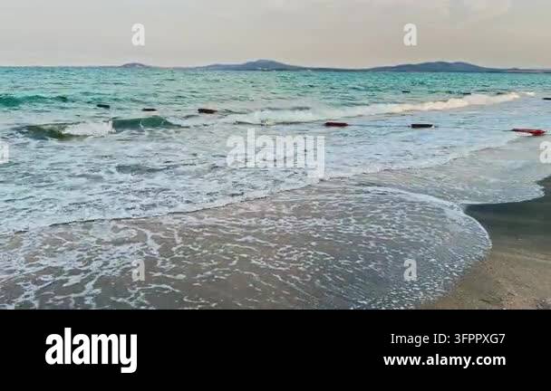 Whased Colors Waves wash onto the sandy shore at a beach. Distant hills can be seen ...