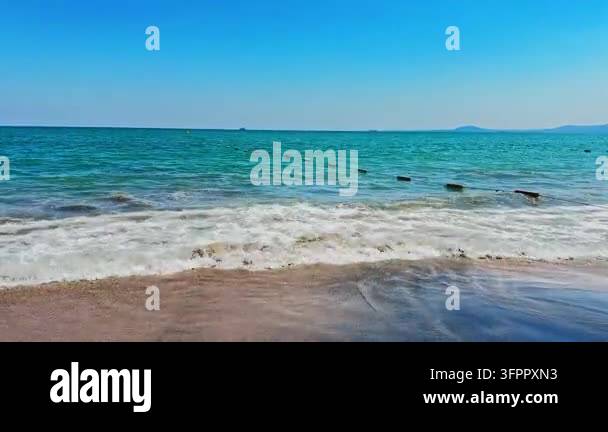 Waves break on a sandy beach under a clear blue sky. The ocean ...