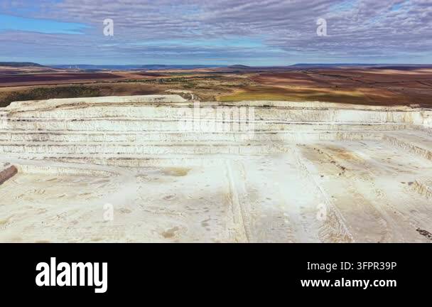 Large Area A wide view of a large open quarry with white rock layers. The quarry ...