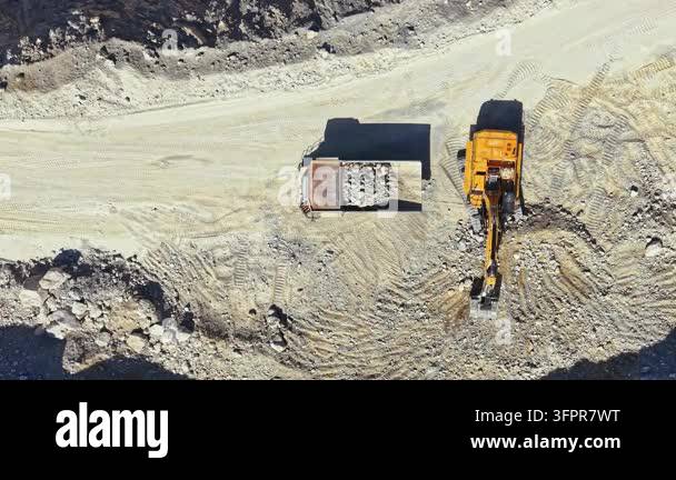 Large Area A large yellow machine loads rocks into a truck at a construction site ...