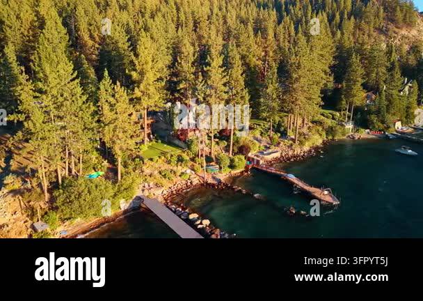 Lakeside homes and docks beneath a dense Lake Tahoe forest. Sunlight ...