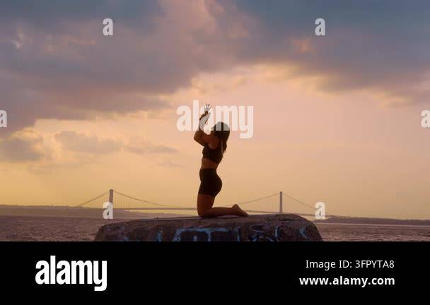 Woman doing kneeling backbend yoga exercise at sunset in New York. Side ...