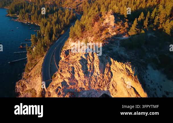 Road cut into a lakeside cliff beside conifer forest. A curving road ...