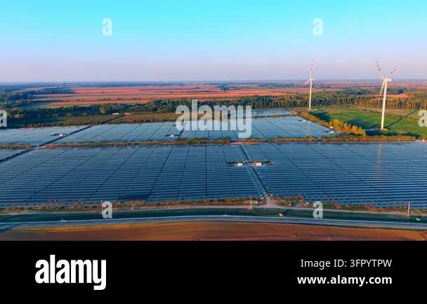 Solar farm and wind turbines, aerial view across panel rows. Blue ...