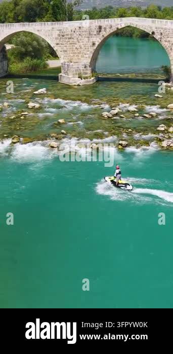 Multiarch Bridge A personal watercraft rider moves through turquoise river water beneath ...