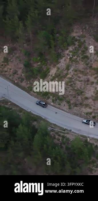 Aerial view follows vehicles traveling along a winding road through ...