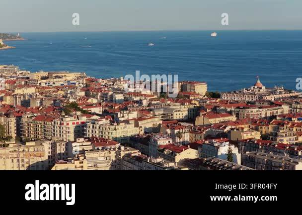Slow telephoto sideways move over red rooftops toward Baie des Anges ...