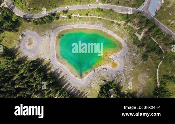 Static top-down drone hover over vivid turquoise alpine lake with rocky ...