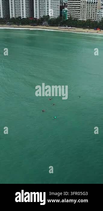 Surfers paddle and ride small waves offshore beside a sandy beach and ...