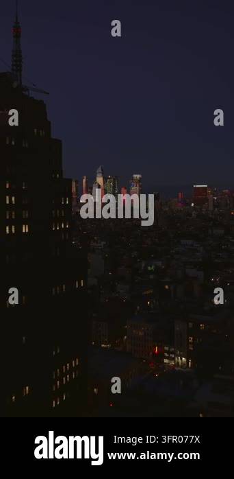 Vertical video: Fly above night city. Passing by tall office building ...