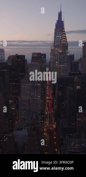 Vertical video: Forwards fly above city at dusk. Illuminated iconic ...