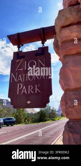 A Zion National Park sign hangs from a timber beam. Sunlight shines ...
