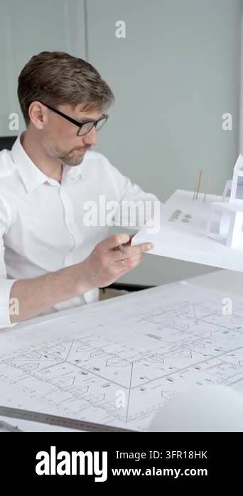 Architect in eyeglasses holding aloft a paper architectural model ...