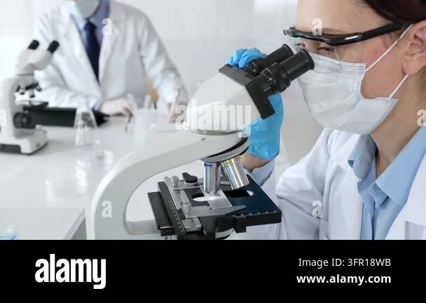Masked professional female scientist examining sample through ...