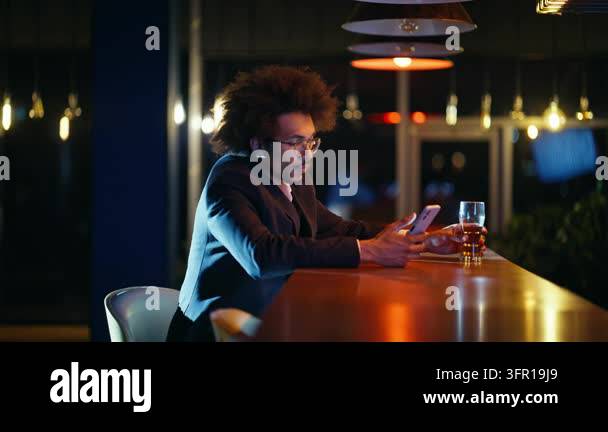 Businessman scrolling smartphone sipping beer bar counter evening ...