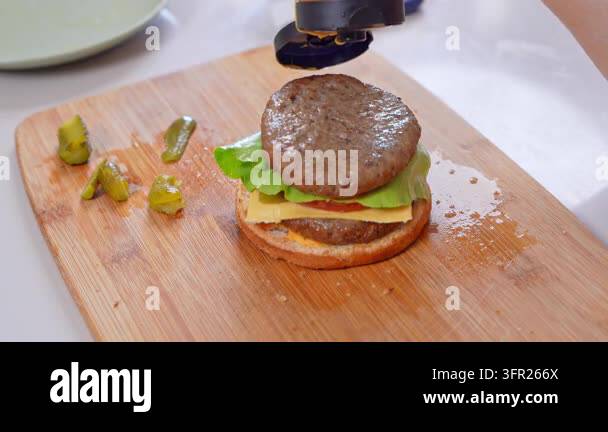 Orange cheese sauce squirts from a bottle onto a grilled beef patty ...