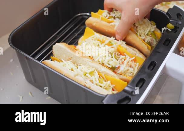 A hand places another bun topped with shredded cheese, sliced cheddar ...