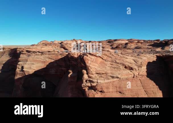 Person standing on rocky cliffs under a clear blue sky in a desert ...