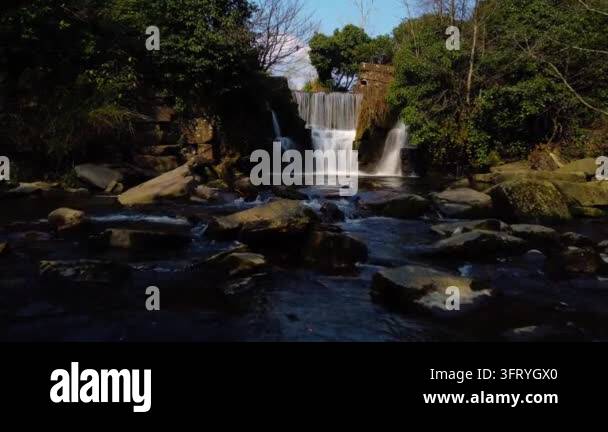 Waterfall cascading over rocks into flowing stream surrounded by trees ...