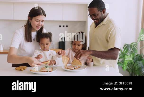 Happy interracial couple making sandwiches together with little kids at ...