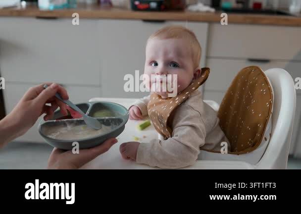 A side view of a cute little baby sitting in a high chair while being ...