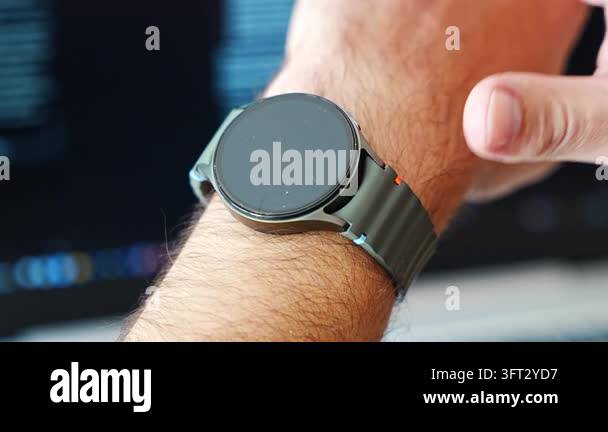 Fingers reach to tap a round smartwatch with an olive green strap on a ...