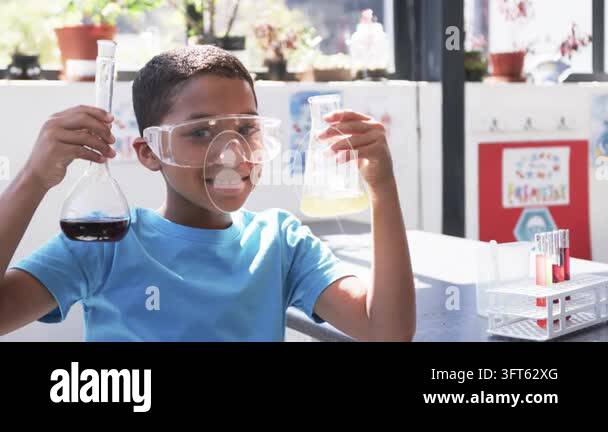 Boy holding two flasks in science lab, tilting right flask, causing ...