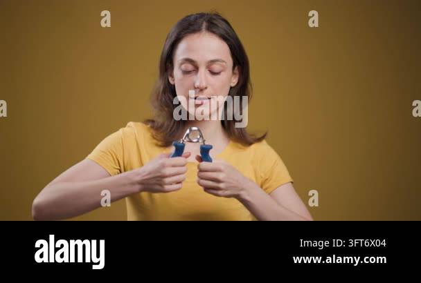 Focused young woman in a yellow t-shirt using a hand gripper to enhance ...