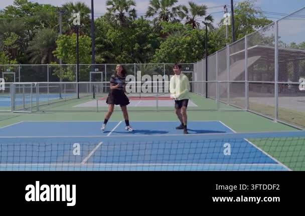 Back Outside Two young people playing pickleball on an outdoor court, hitting the ...
