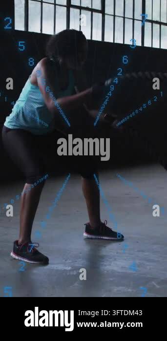 Woman doing battle-rope in warehouse gripping rope, driving waves as ...
