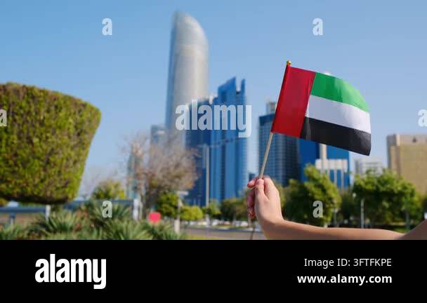 Female hand holding small UAE flag against Abu Dhabi skyline. Symbol of ...