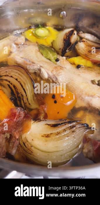 A chef prepares a traditional hot soup base, cooking chicken stock in a ...