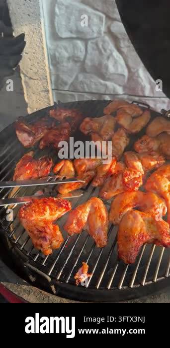 Chef turning seasoned chicken wings with tongs on BBQ outdoor grill ...