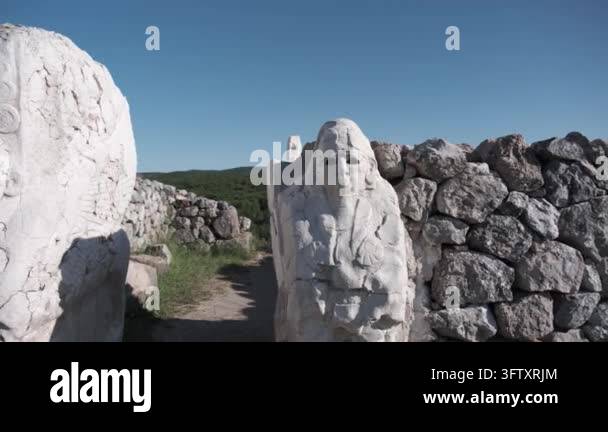 Ancient stone statues stand guard beside a weathered stone wall under a ...
