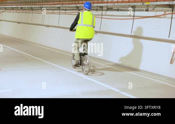 Worker in safety gear rides a bicycle through a technical CERN tunnel ...