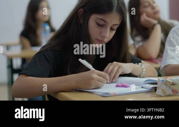 A young girl concentrates on her studies while taking notes at a desk ...
