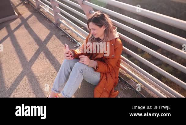 Blonde woman in brown jacket talks on videocall as sits on urban ...