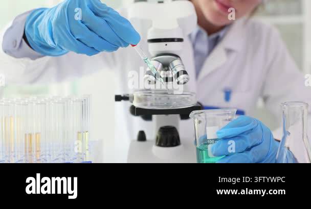 Woman assistant drips blue liquid onto microscope slide in medical lab ...