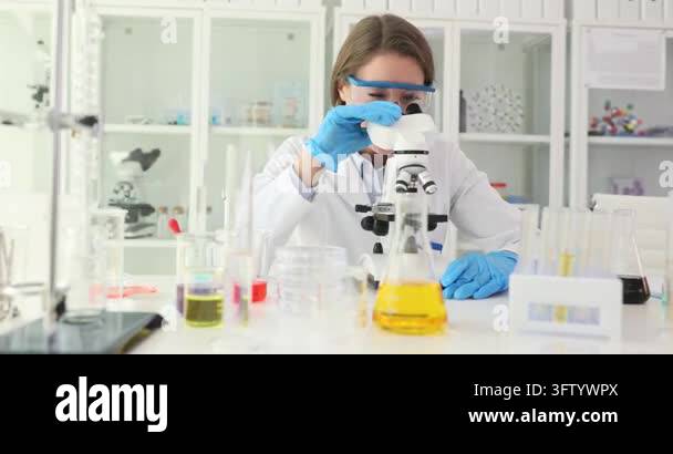 Friendly woman scientist stops looking in microscope and waves hand in ...