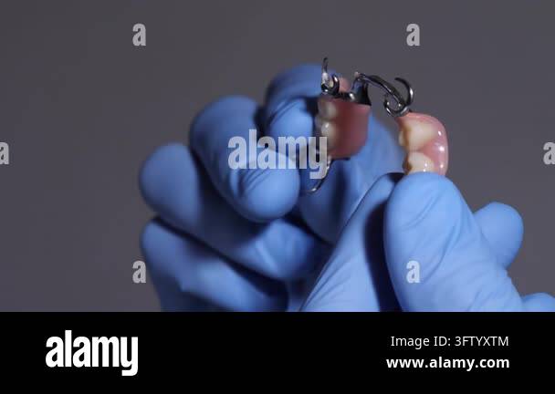 A dental professional in blue gloves displays a dental prosthesis ...