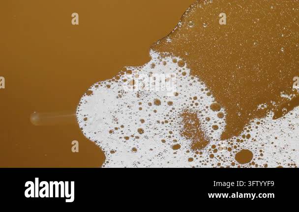 Sudsy white foam expanding and contracting over a golden-brown liquid ...