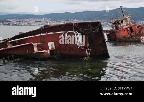 Abandoned rusty red fishing boat partially submerged in the waters of ...
