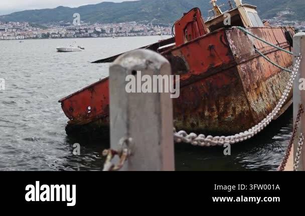 Abandoned rusty red fishing boat partially submerged in the waters of ...