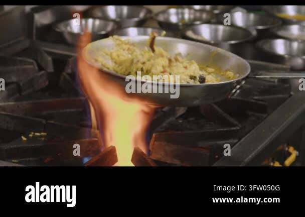 Chef flambeing food in a pan over a gas stove with flames, cooking in a ...
