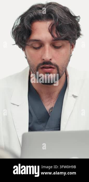 Vertical video showing a man wearing a white lab coat and grey scrubs ...