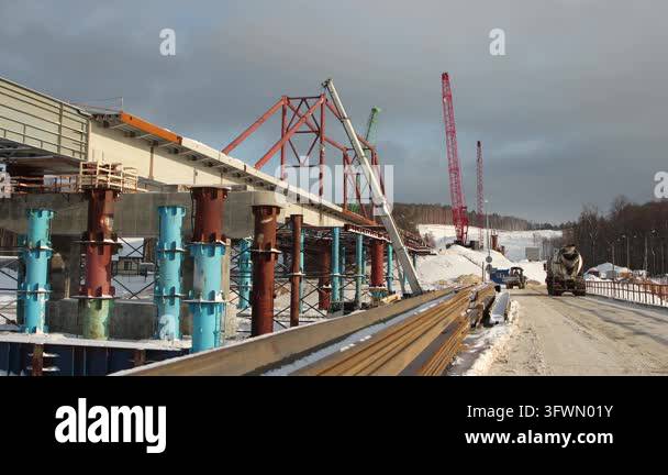 Workers continue building a bridge in a snowy location. Cranes lift ...