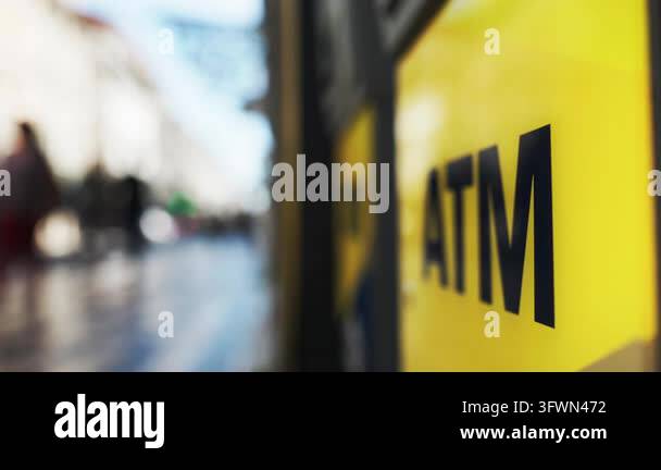 Close-up of a yellow atm sign with a blurred city street and anonymous ...